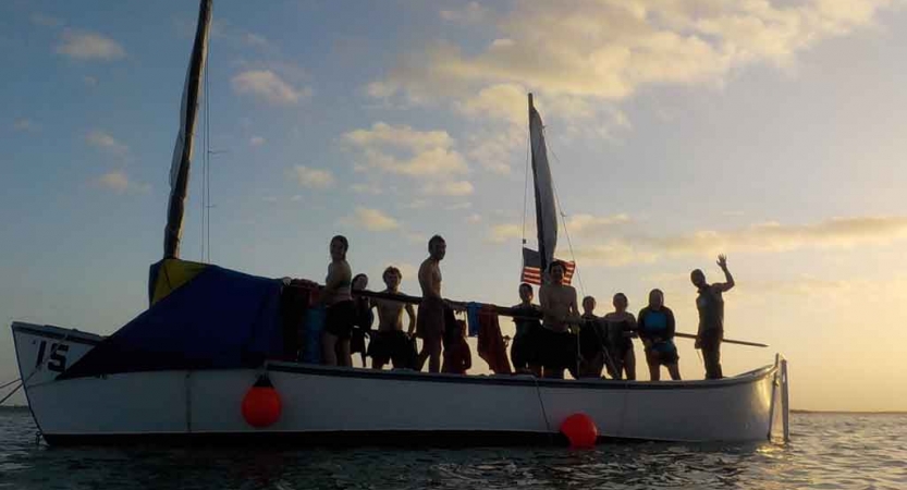 the silhouette of a group of people on a sailboat at sunset